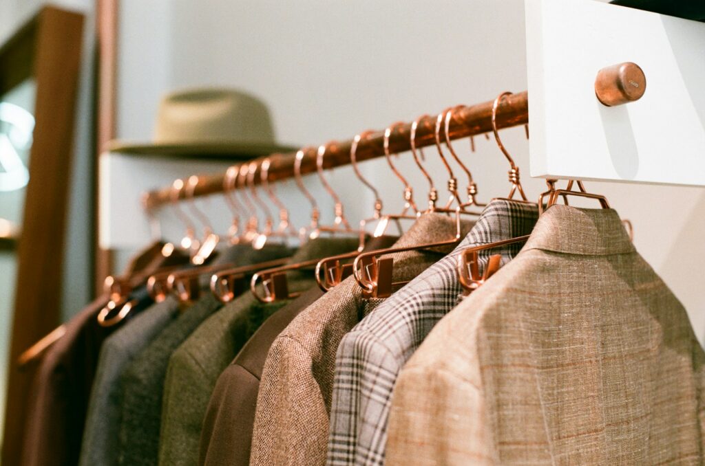 Curated boutique wardrobe rack with tailored tweed and linen blazers hanging on warm copper hangers