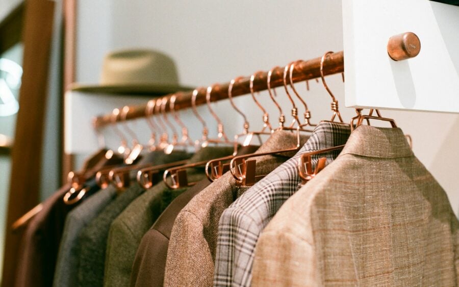 Curated boutique wardrobe rack with tailored tweed and linen blazers hanging on warm copper hangers