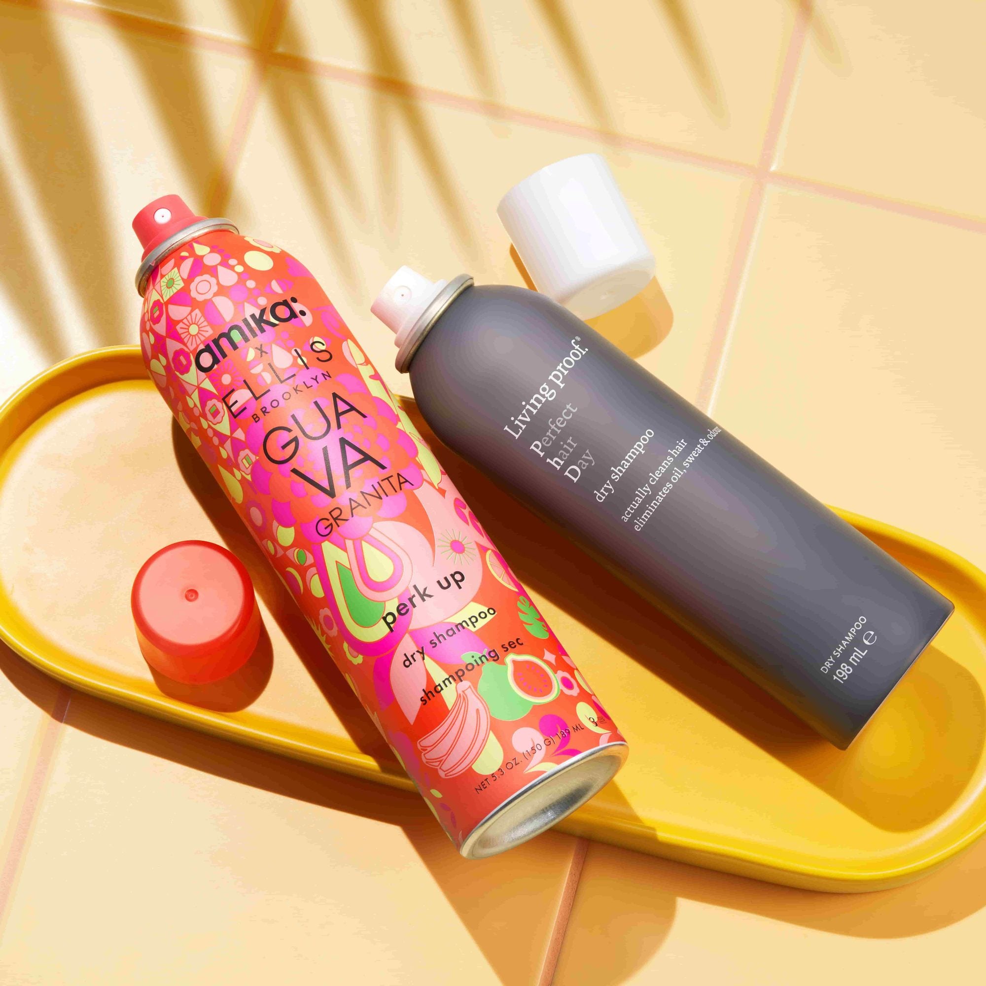 Colorful patterned dry shampoo spray and dark cylindrical hair product on yellow tray with red cap
