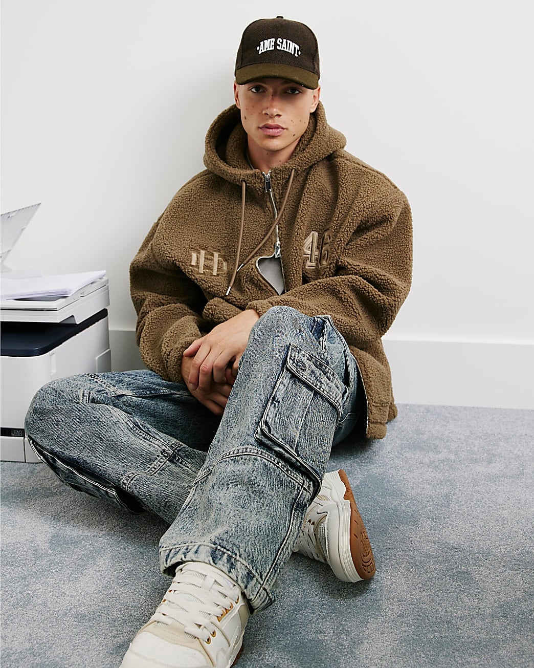 Person in olive green fleece hoodie and vintage blue jeans sitting on floor wearing white sneakers
