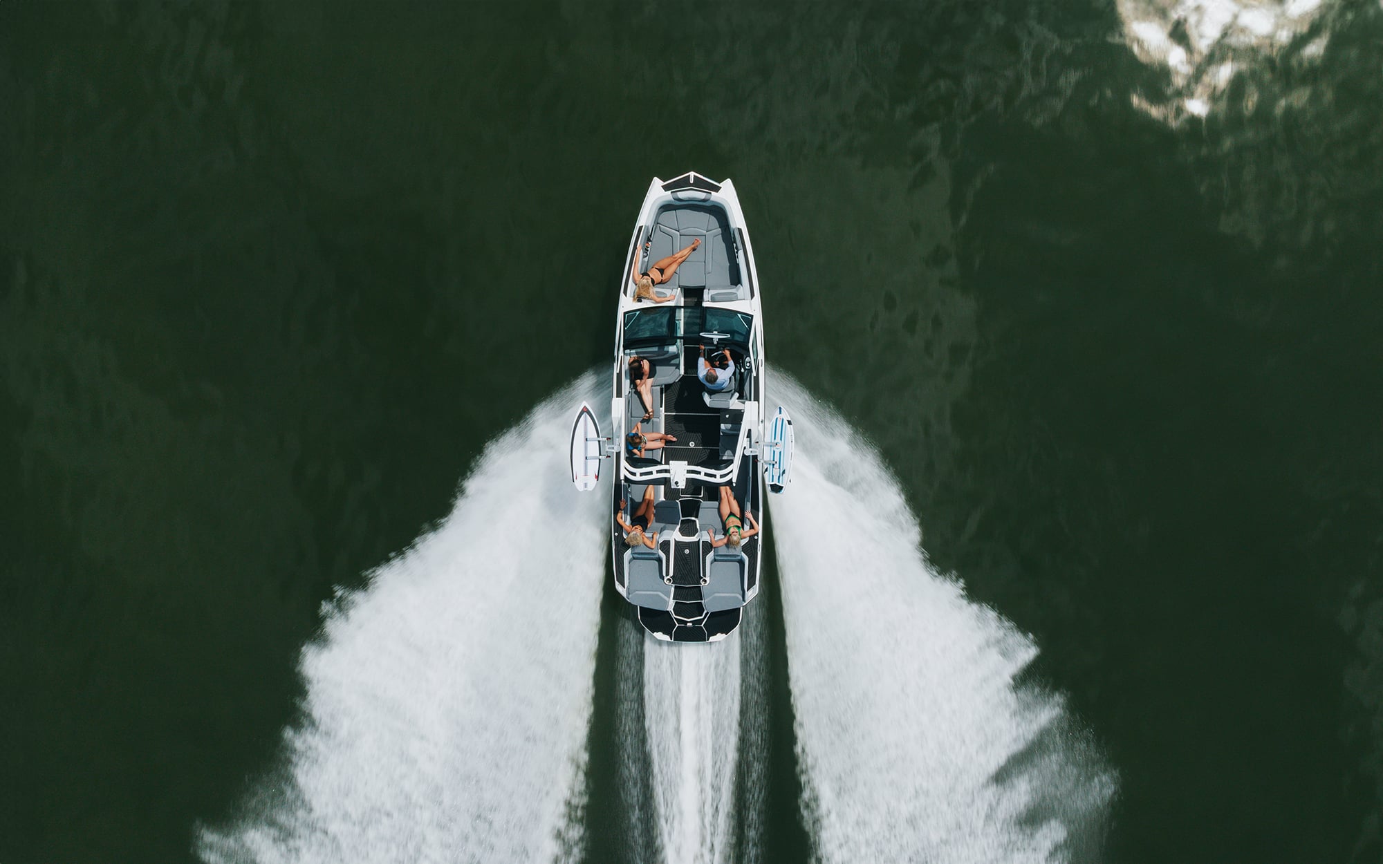 Overhead view of white speedboat with passengers creating wake spray through green water between forested shores