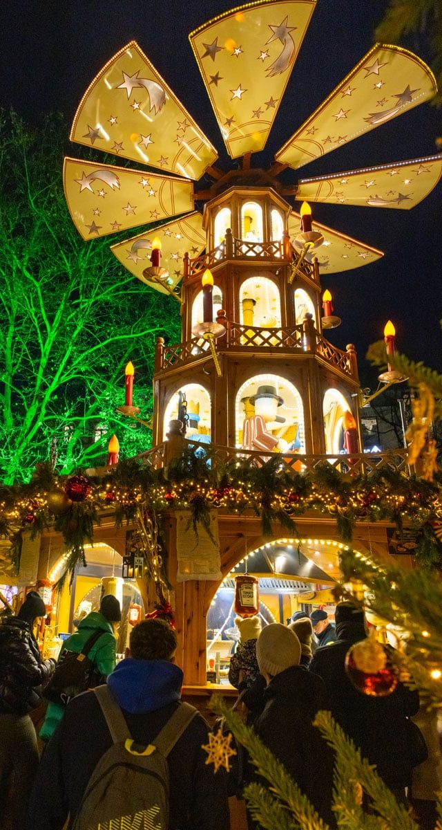 Illuminated Christmas pyramid decoration with golden star panels and nativity scenes at night market
