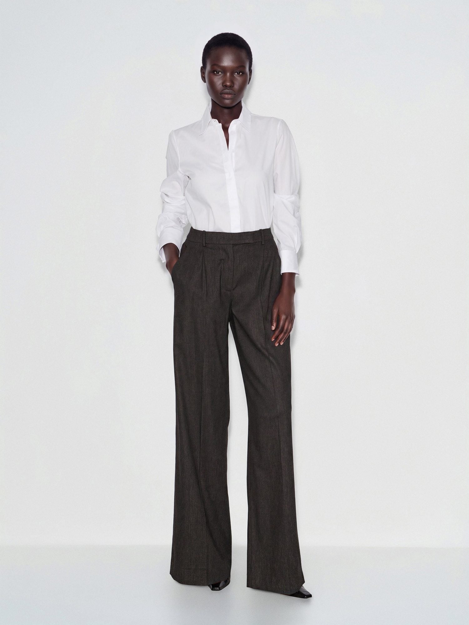 Woman in white button-up shirt tucked into charcoal wide-leg trousers with black slip-on shoes