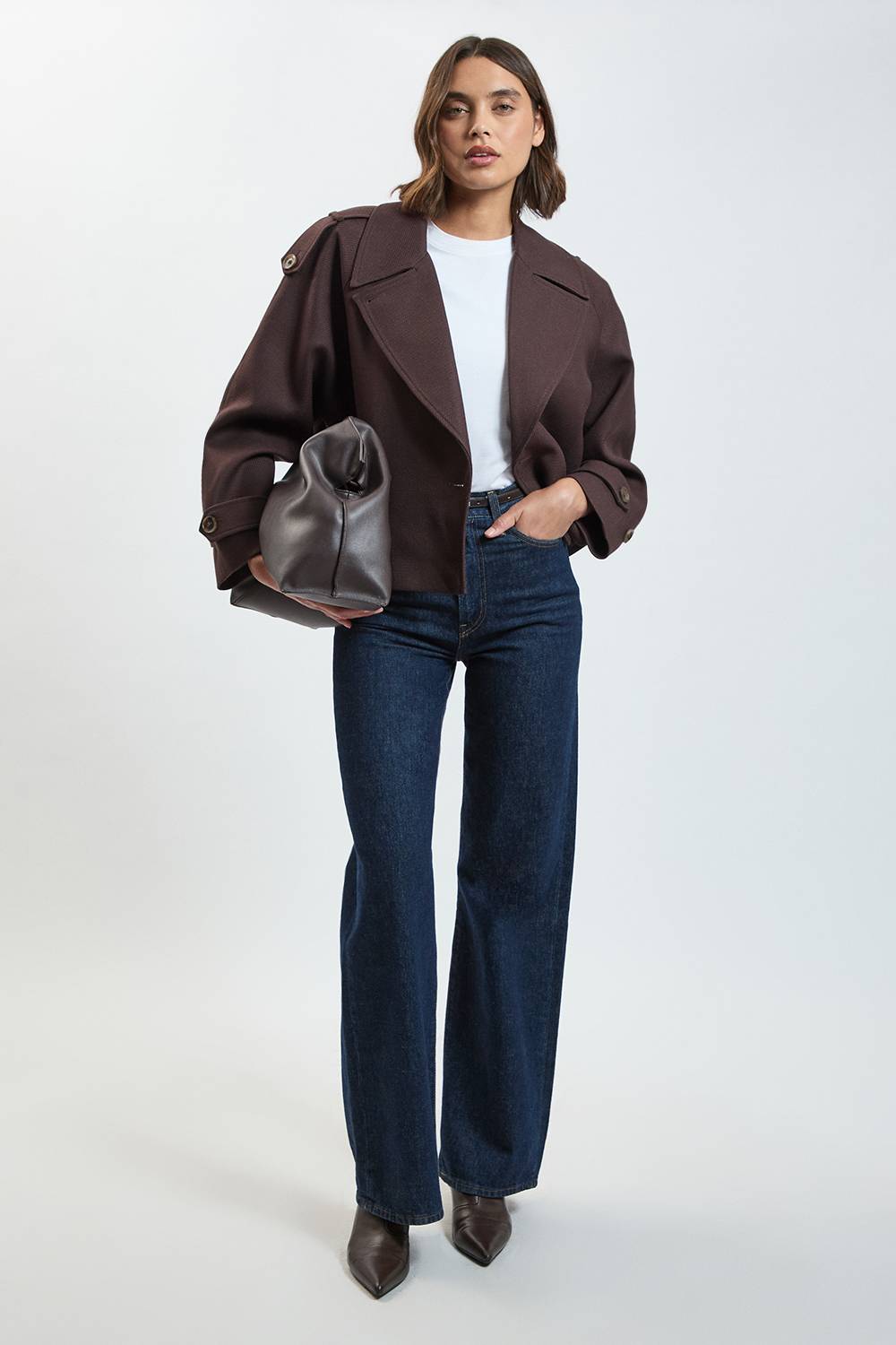 Woman wearing brown oversized blazer with white shirt, dark jeans, and carrying a leather shoulder bag