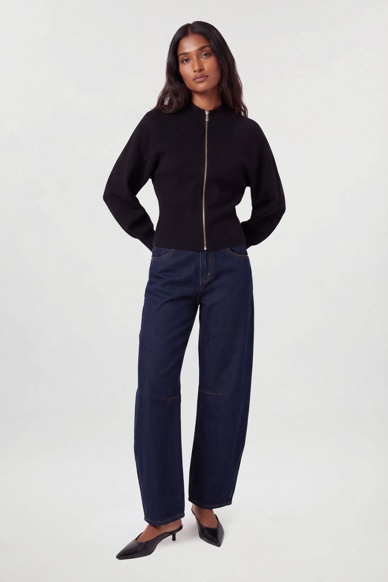 Woman wearing black zip-up knit sweater with dark navy wide-leg jeans and black kitten heels