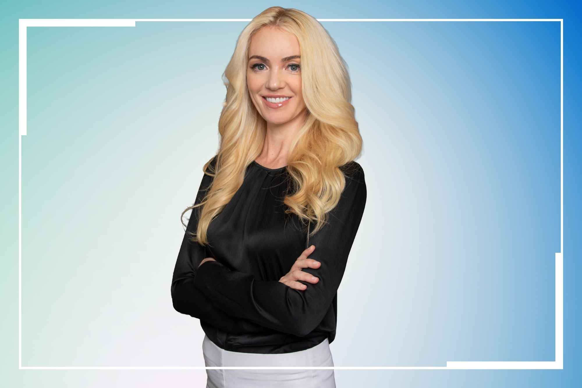 Professional portrait of blonde woman in black long-sleeved top and white pants smiling with arms crossed against turquoise to blue gradient background