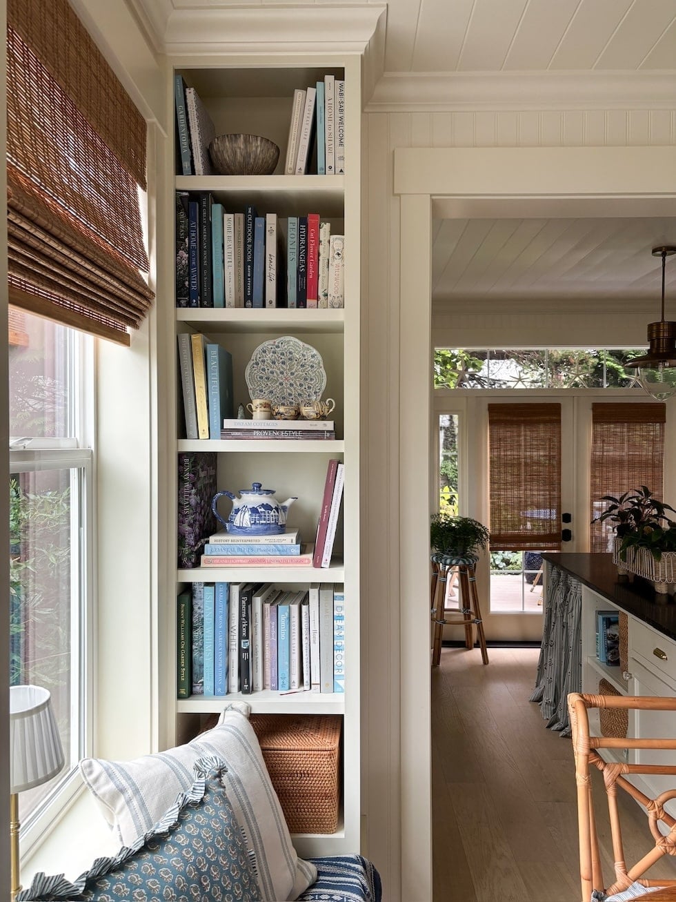 Built-in white shelving filled with books, decorative objects, and woven basket near window seat with striped pillow