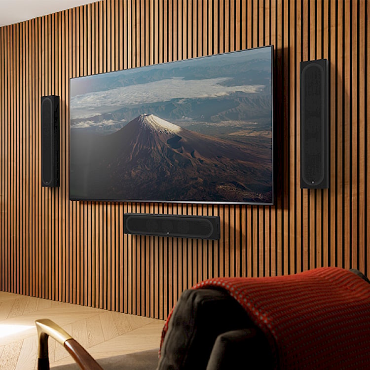 Flat-screen TV displaying mountain landscape mounted on wooden slat wall with soundbar and speakers below
