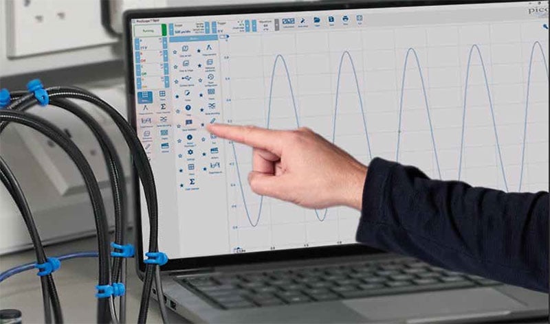Hands pointing at laptop screen showing repetitive waveform signal patterns with software toolbar visible and cables with blue connectors in foreground