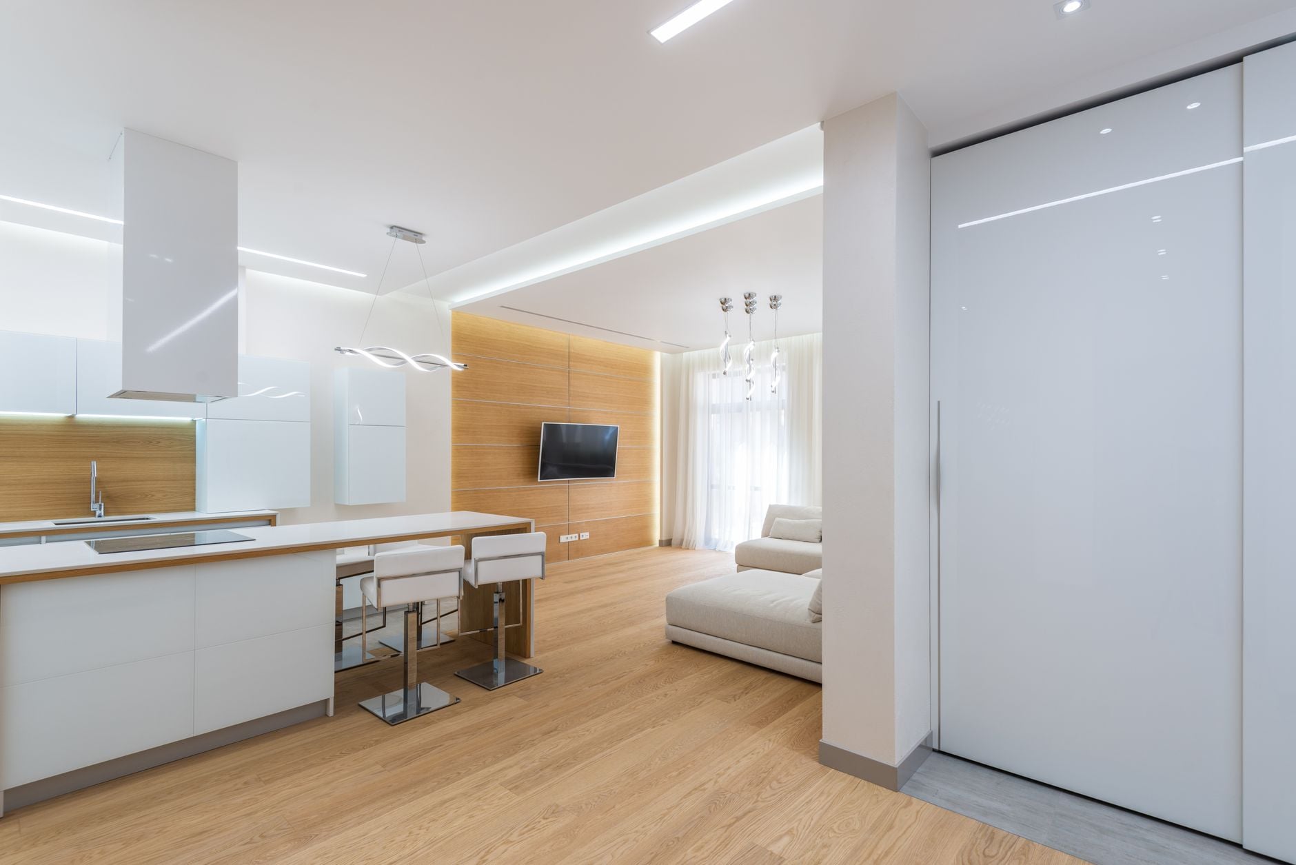 Modern open-plan studio apartment with white kitchen, wooden accent wall, and beige seating area