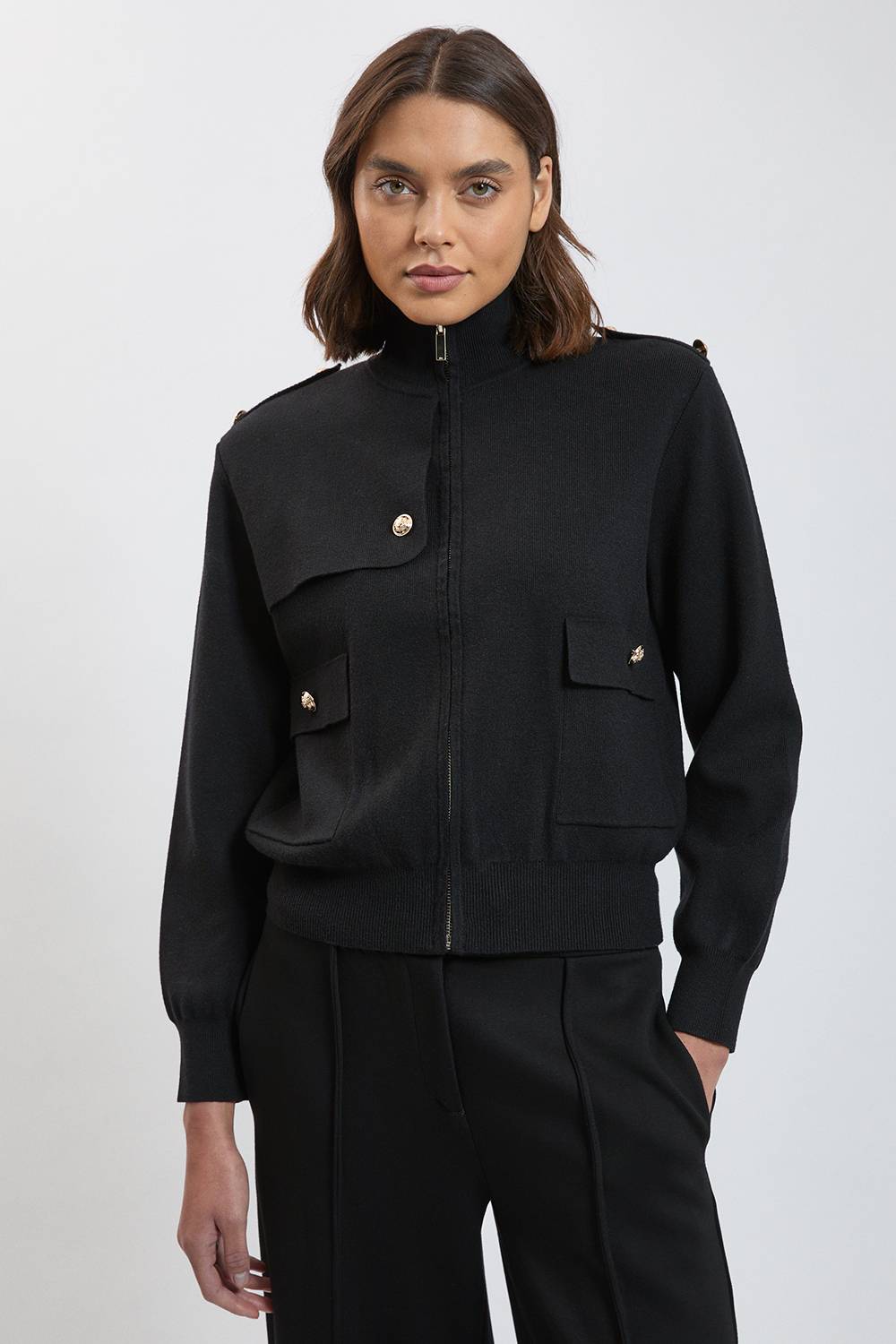 Woman wearing black knit zip-up cardigan with chest pockets and black trousers