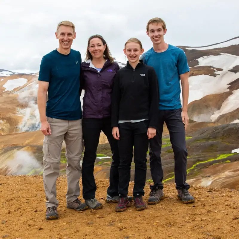 Four people smiling at a geothermal mountain landscape with steaming vents and patches of snow