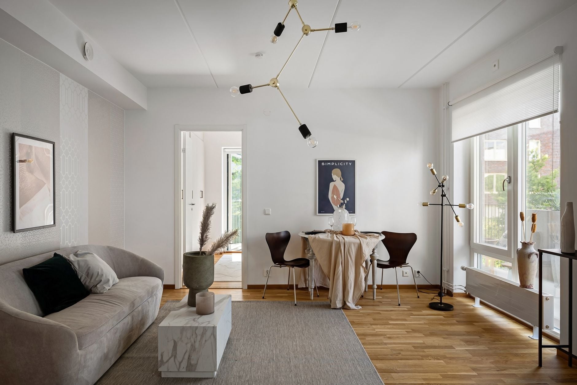 Minimalist living space with curved gray sofa, round dining table, and brass pendant lighting fixtures