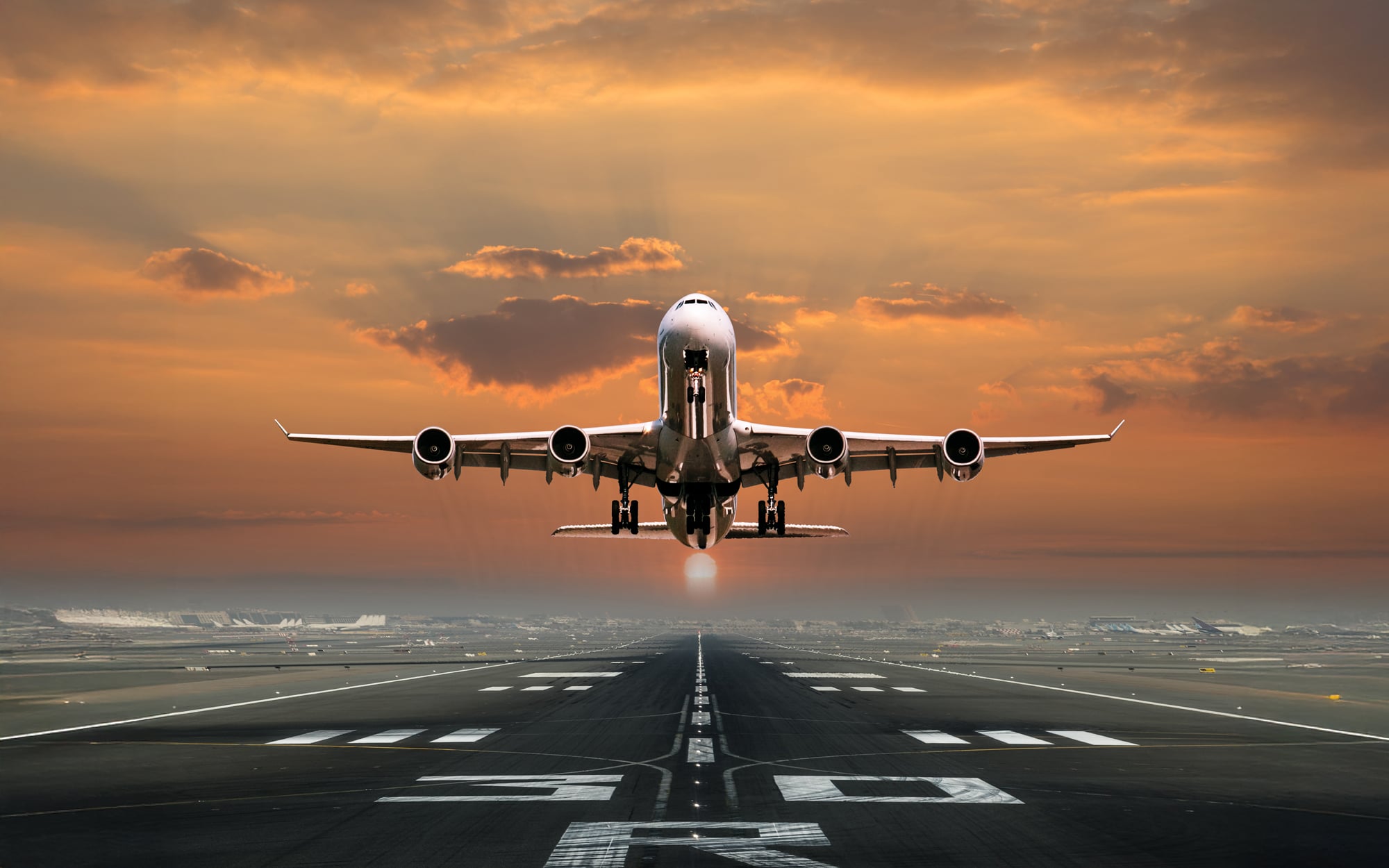 Commercial aircraft on final approach to runway at sunset with golden sky and clouds