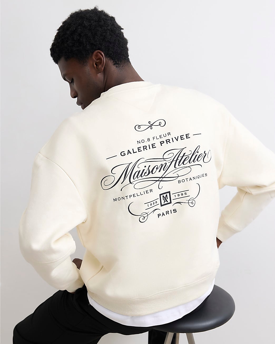 Person wearing cream sweatshirt with decorative back print featuring ornate text and flourishes