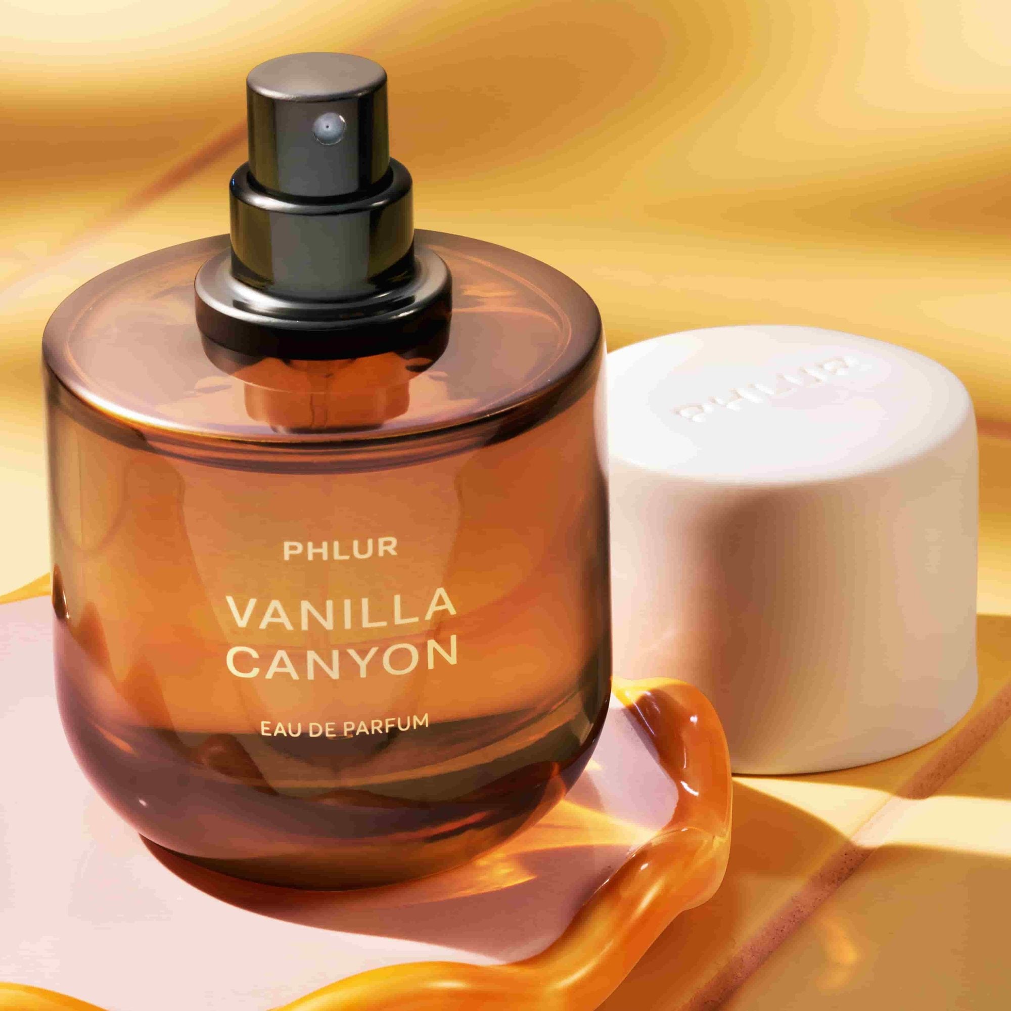 Amber perfume bottle with black spray cap and white cylindrical cap beside it on golden background