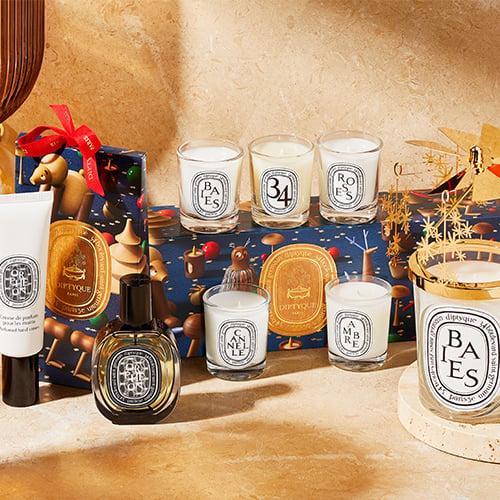 Collection of white and dark glass candles with gold accents and matching perfume bottles on neutral background